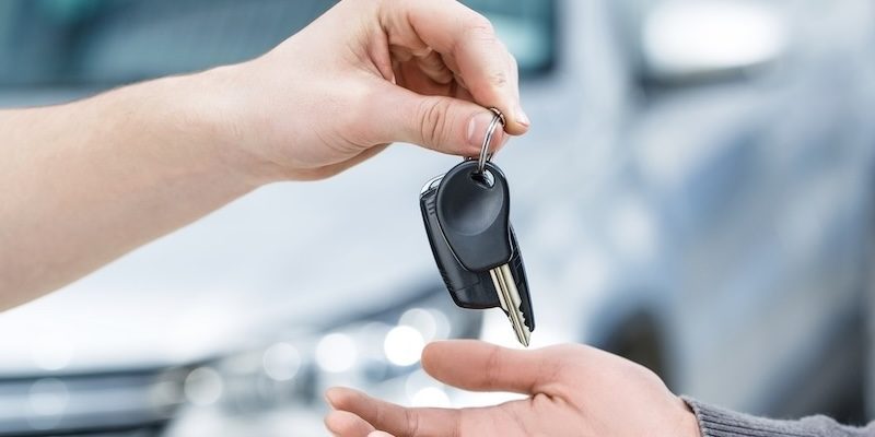 A dealership salesman hands over the keys to a used vehicle.