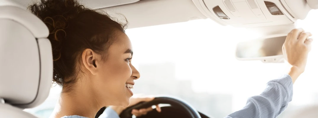 A young driver repositions the review mirror while test driving a used vehicle.