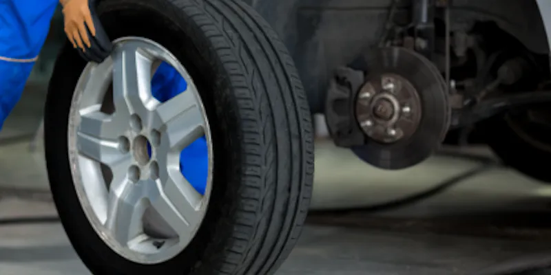 A technician rolls a tire away from a raised car.