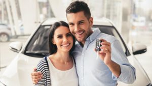 happy_couple_smiling_in_front_of_new_white_car_in_dealership