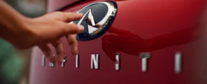 Person touching the INFINITI logo on the outside of the 2025 INFINITI QX55.
