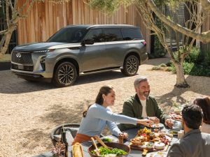 People sitting on picnic table in front of parked 2026 INFINITI QX80