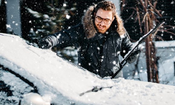 portrait of smiling man cleaning snow off his car during winter snowfall