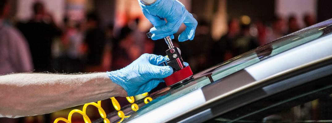 An individual wearing blue gloves repairing a crack or chip in a car's windshield.