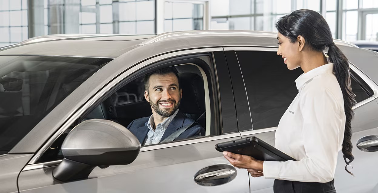 Sales person speaking to customer sitting inside vehicle