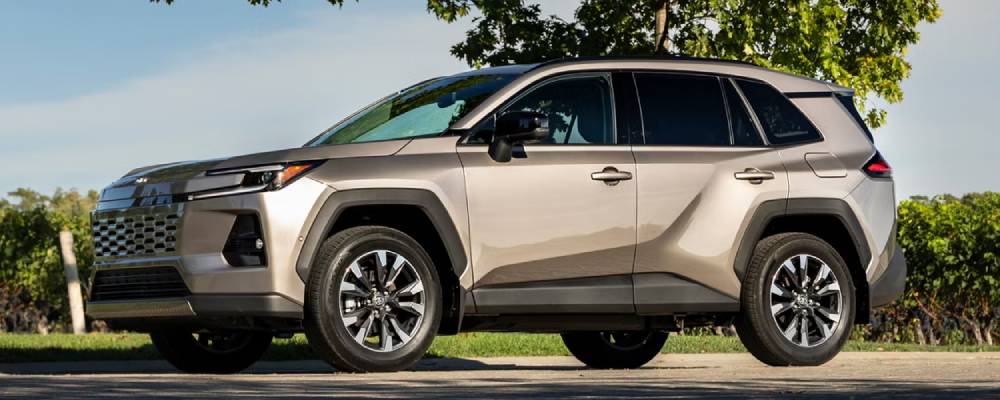 A gold 2026 Toyota RAV4 parks in front of a green lawn with a tree in the background